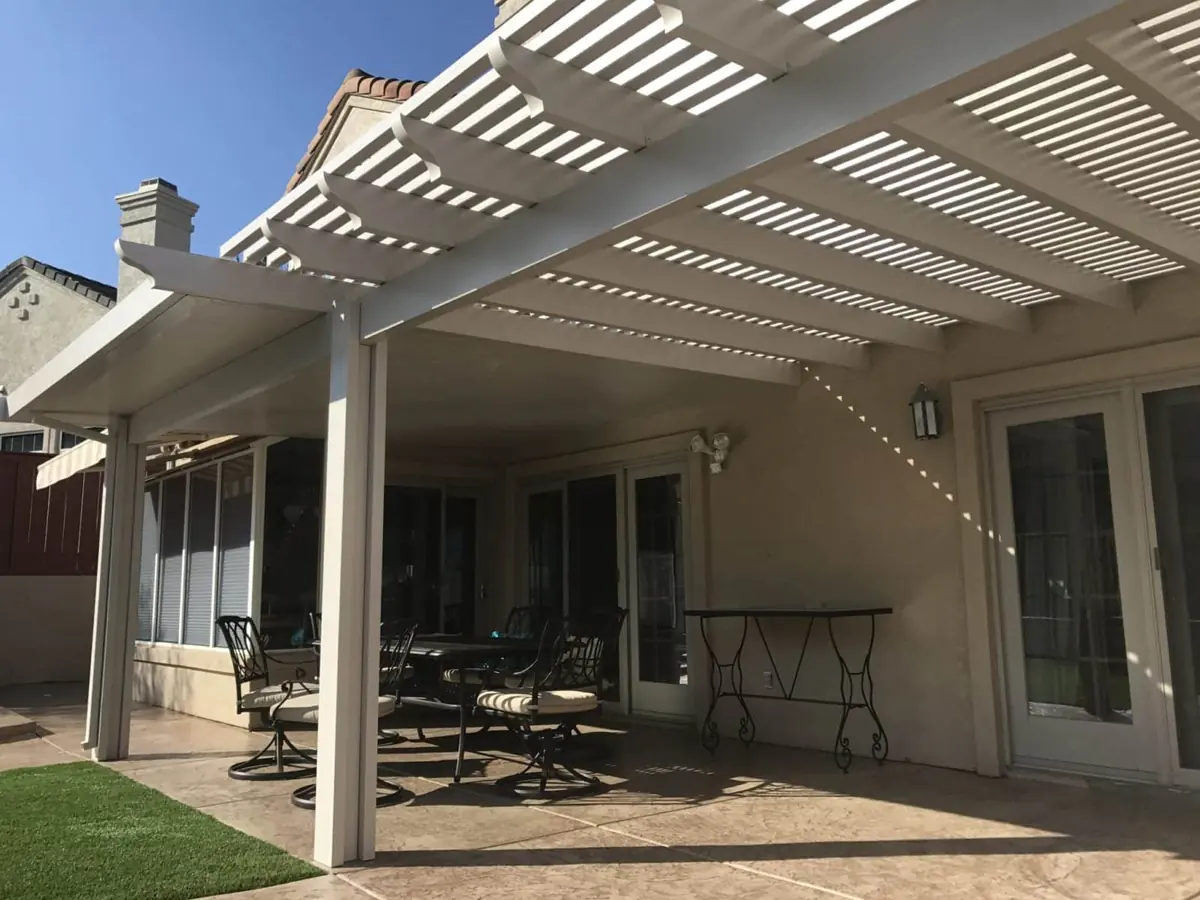 White aluminum lattice patio cover attached to a two-story home, shading a dining set